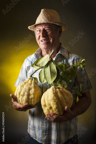 Happy farmer keep in his hands two giant cedars fruit. Studio portrait, yellow and black background photo