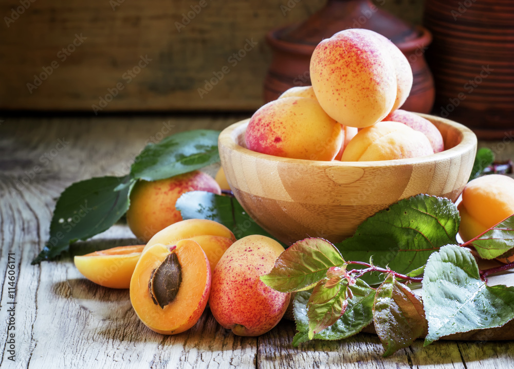 Fresh apricots with leaves in a bowl, vintage wooden background,