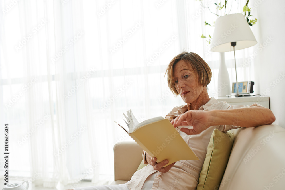 Pretty aged woman sitting on sofa and reading a book Pretty aged woman sitting on sofa and reading a book