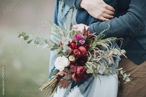 Wedding. mountains. bride's bouquet. Artwork. Grain. Guy hugs a girl in a dress on a background of mountains, a girl holding a bouquet of red flowers, white flowers and greenery