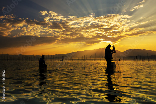 Silhouettes of the traditional fishermen throwing fishing net during sunrise, Thailand