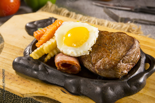 Beefsteak on iron plate with egg and carrot on the table in restautrant photo