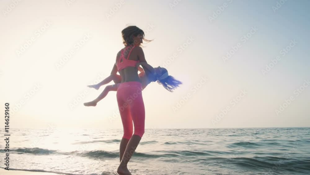 Young mother with her little daugter having fun on the beach near the water