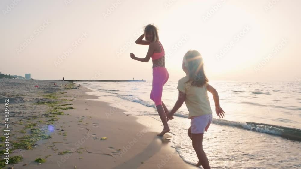 Young mother with her little daugter running on the beach near the water, slowmo