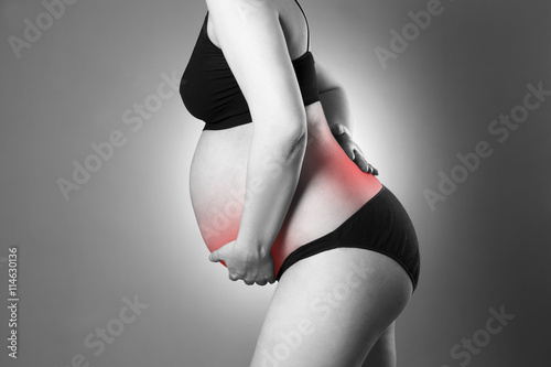 Caucasian pregnant woman in black lingerie with back and abdominal pain on gray studio background photo