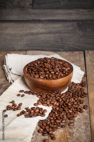 Roasted coffee beans in a wooden bowl on wooden background