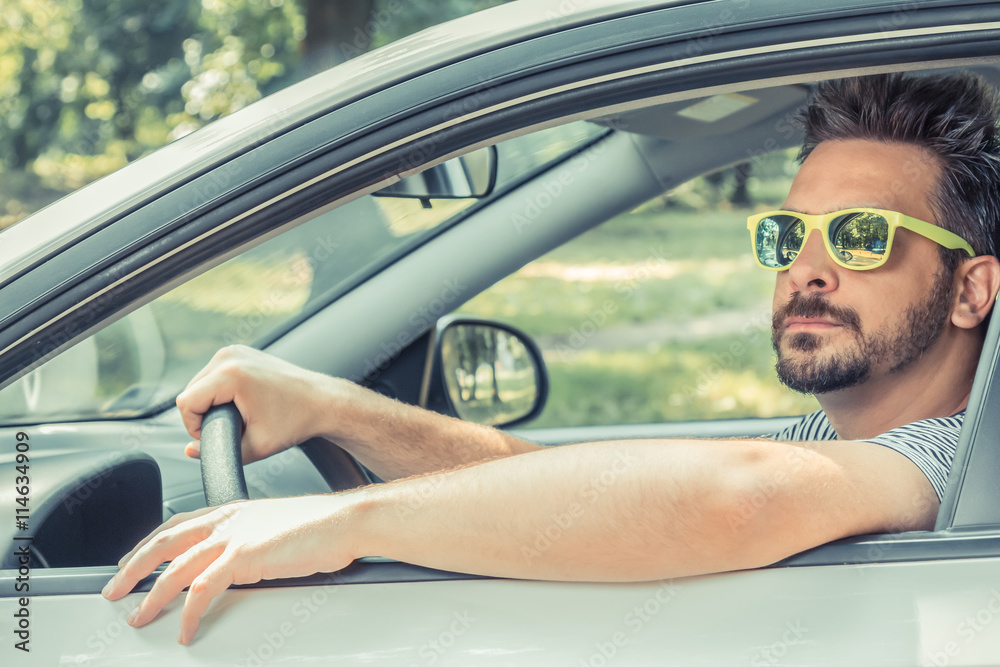 Naklejka premium Portrait of young driver wearing sunglasses in driver’s seat. Vacation and travel concepts.
