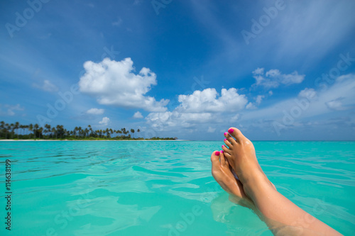 Close-up of female foot in the blue water on the tropical beach.