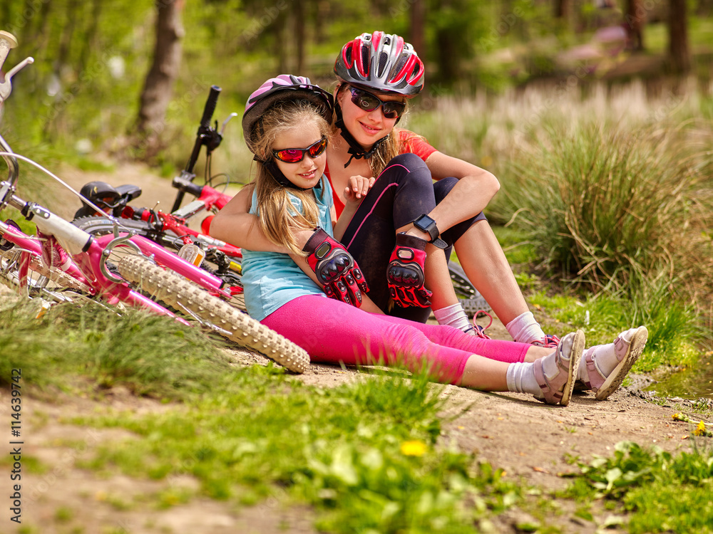 Obraz premium Bikes cycling family. Happy mother and daughter are sitting on road near bicycles. Cycle racing concept.