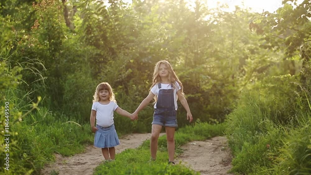 Two cheerful sisters. Cute girls walking in the park hand in hand. Family values. Two cheerful sisters. Cute girls walking in the park hand in hand. Family values.