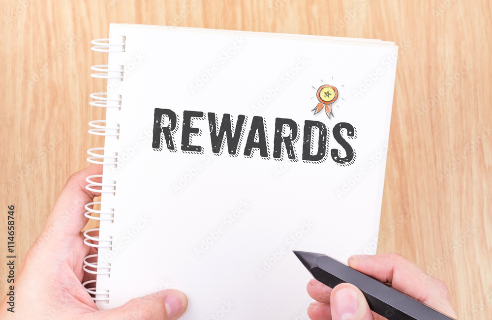Rewards word on white ring binder notebook with hand holding pen