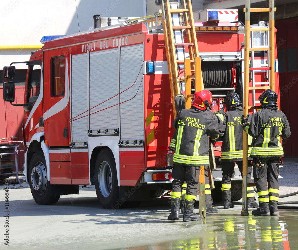 Naklejka premium firefighters in action take the wooden ladder from the firetruck