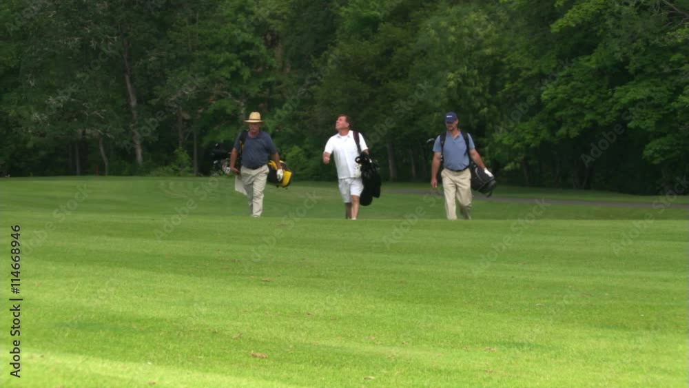 Three golfers carrying their bags and walking toward camera across a hilly course Three golfers carrying their bags and walking toward camera across a hilly course