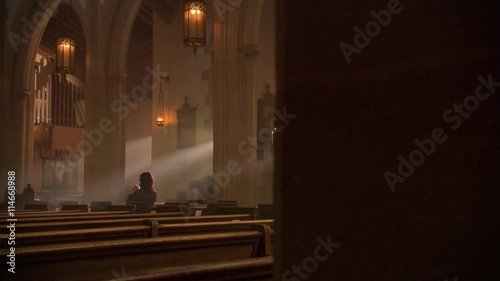 Woman kneeling and praying in sunlit nave of a Catholic church