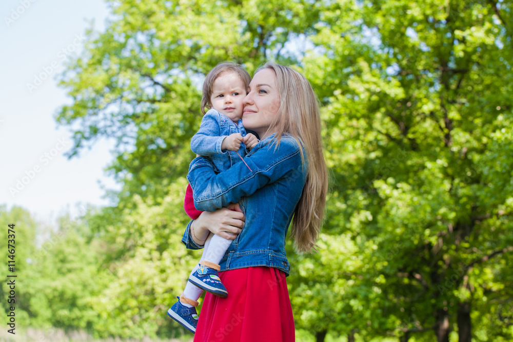 Fototapeta premium Mom and daughter in the same dresses sitting on the ground in the grass