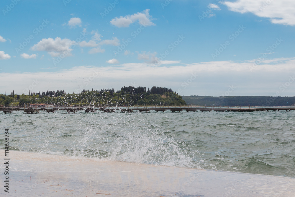 Waves crashing by seaside promenade against the blue sky.