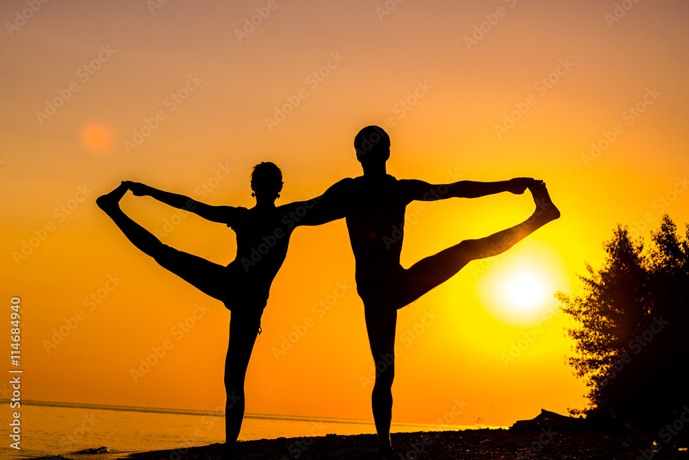 An attractive young woman and man doing yoga on the beach, Sea