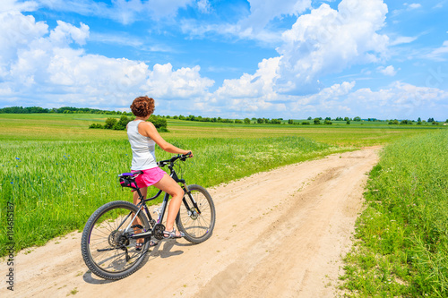 Young attractive woman riding a bike on rural road in green summer landscape, Poland