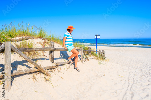 Young woman tourist standing at entrance to beautiful sandy beach in Lubiatowo coastal village, Baltic Sea, Poland