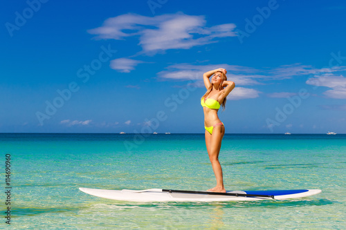 Happy beautiful young girl with paddle board on a tropical beach