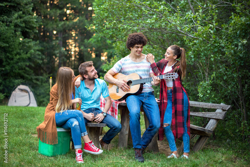 Young people having fun in nature. Handsome man playing a guitar to his friends. Soft focus, high ISO, grainy image. 