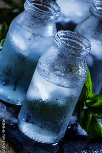 Very cold mineral water with ice in a misted glass bottles, dark