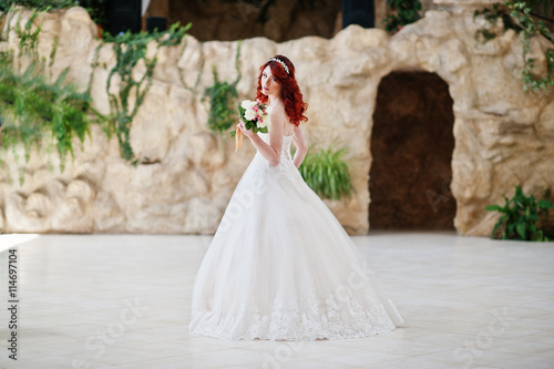 Charming red-haired bride with wedding bouquet at hand posed at