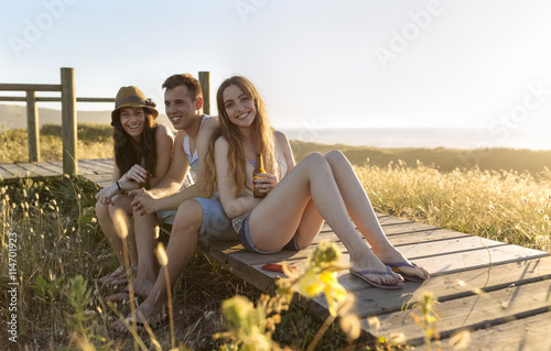 Friends sitting on boardwalk at the beach, drinking beer at sunset photo