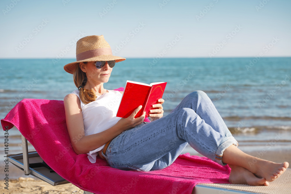 Relaxing on the beach. Beautiful woman reading a book at seaside. 