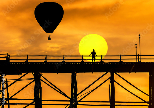 silhouette hot air balloons floating over old wooden bridge in sangklaburi, kanchanaburi,  thailand on sunset background  photo