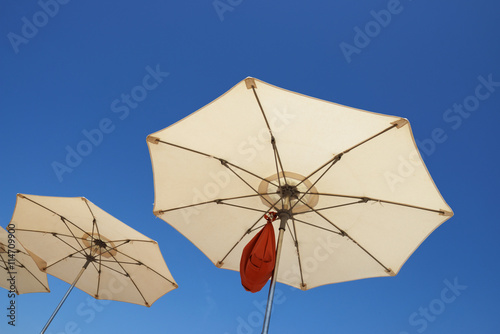 Beach parasols are on bright blue sky background.