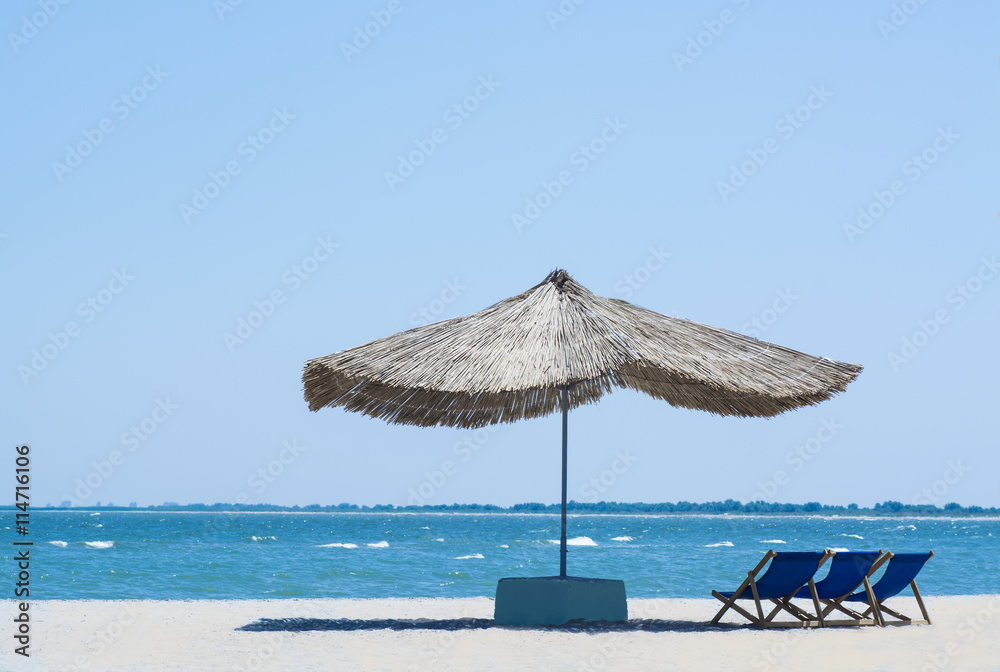 Beach straw umbrella from the sun on the beach with sun beds, on the background of the sea and blue sky Beach straw umbrella from the sun on the beach with sun beds, on the background of the sea and blue sky