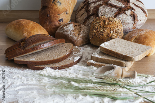 Verschiedene Brotsorten / Verschiedene Brotsorten und Getreideaehren auf einem Holztisch mit Mehl.