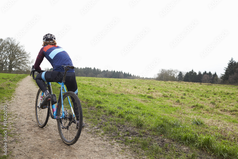 Male cyclist pauses on bike in open countryside, back view