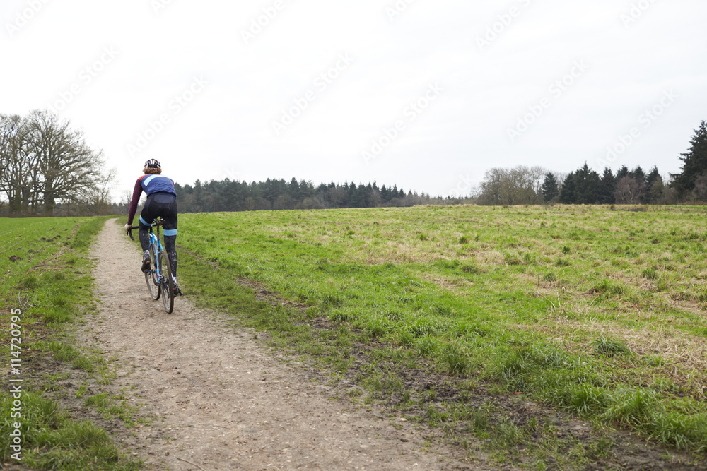 Cross-country cyclist on a path in countryside, back view