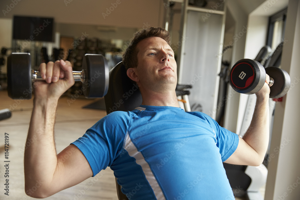 Man works out with dumbbells on a bench at a gym, front view Man works out with dumbbells on a bench at a gym, front view