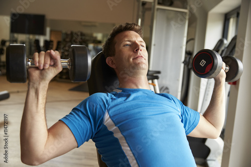 Man works out with dumbbells on a bench at a gym, front view