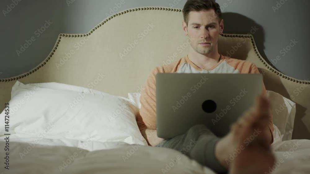 Medium shot of man with coffee using laptop on bed / Cedar Hills, Utah, United States