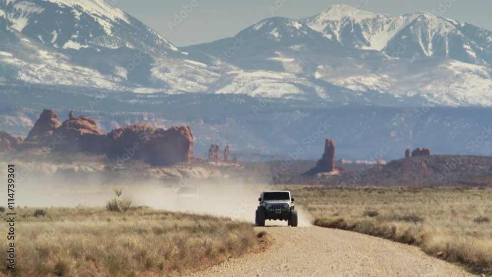 Wide shot of cars approaching on desert road / Arches National Park, Utah, United States