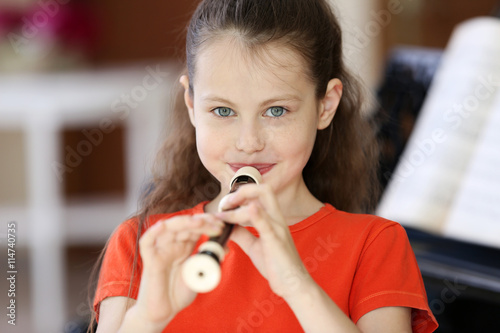 Little girl playing flute on piano background