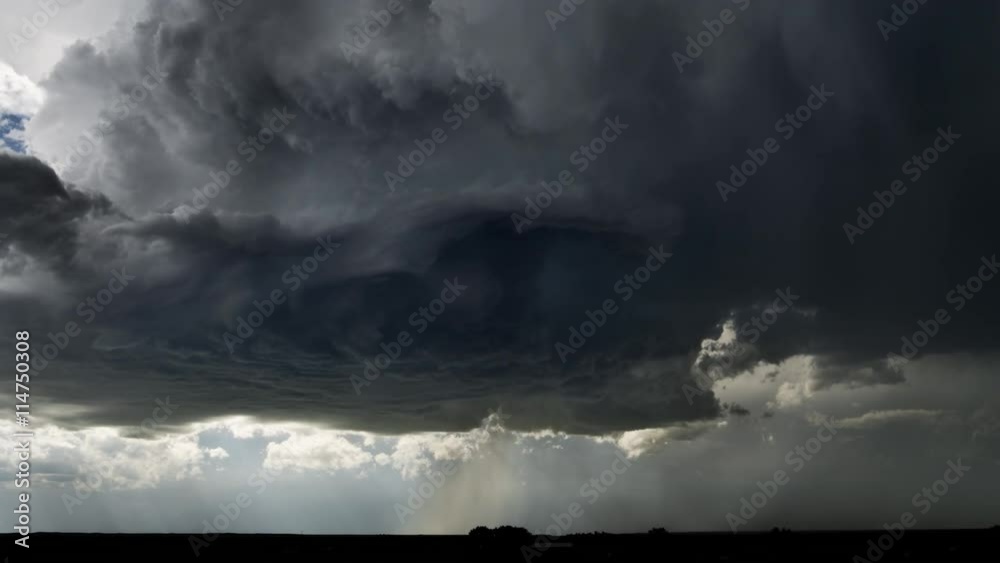High-level base of a thunderstorm showing updraft and rotation, as hail pours onto a dark prairie landscape, time lapse