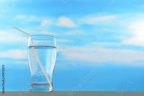 Fresh and clean drinking water in glass with straw on sky background