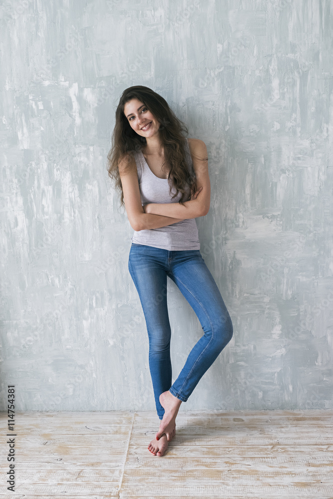 Slim barefoot girl posing against of textured gray wall