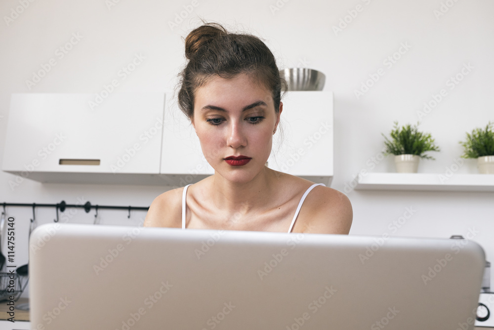 Brunette freelancer looking down on laptop while sitting in kitchen Brunette freelancer looking down on laptop while sitting in kitchen