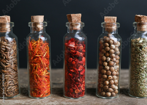 Different spices in small glass bottles on wooden table