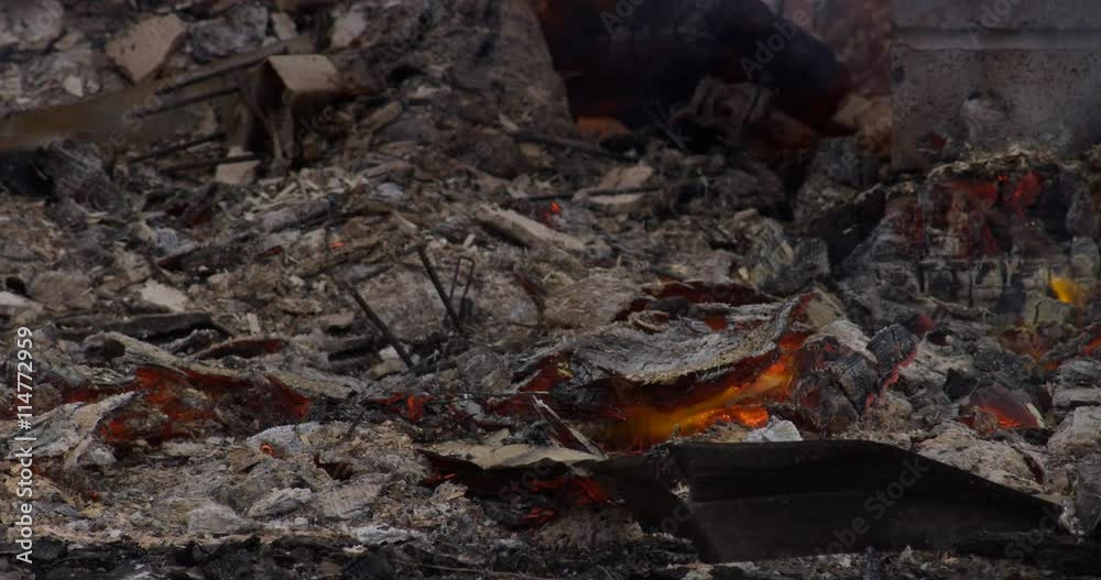 Embers burning underneath a layer of ash amid the rubble of a house fire