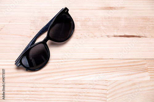 Sunglasses in a top left corner on a light wooden background. La