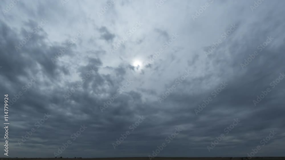 Advancing gray storm clouds hiding the sun over the prairie, time lapse