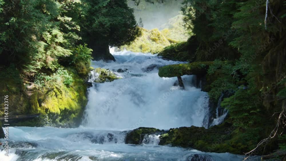 A low waterfall rushing between forested banks A low waterfall rushing between forested banks