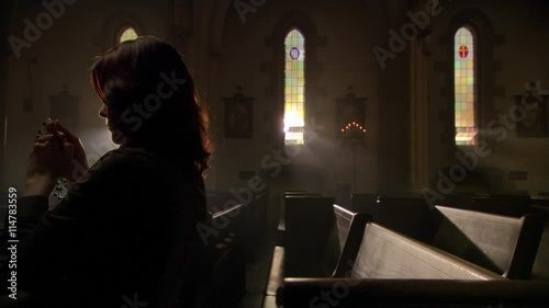 Woman in dimly lit church saying prayers with rosary photo